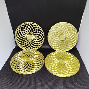 Puede incluir: Cuatro posavasos de metal de color dorado con un diseño geométrico. Cada posavasos presenta un patrón circular de líneas superpuestas que crean un diseño radial.