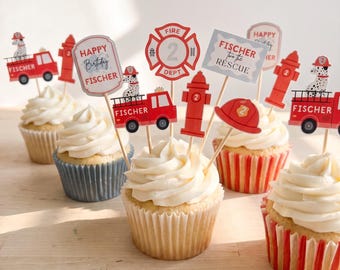 Puede incluir: Un conjunto de cupcakes con adornos de papel que muestran camiones de bomberos rojos, bocas de incendio, perros dálmatas y cascos de bombero. Los adornos incluyen textos como Happy Birthday Fischer, Fire Dept 2 y Fischer to the Rescue.