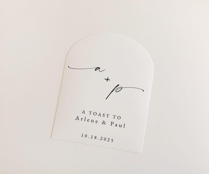 May include: White arched card with black script. The card features the initials "a + p" in elegant cursive, followed by the text "A TOAST TO Arlene & Paul" and the date "10.18.2025". The design is minimalist and suitable for wedding stationery.