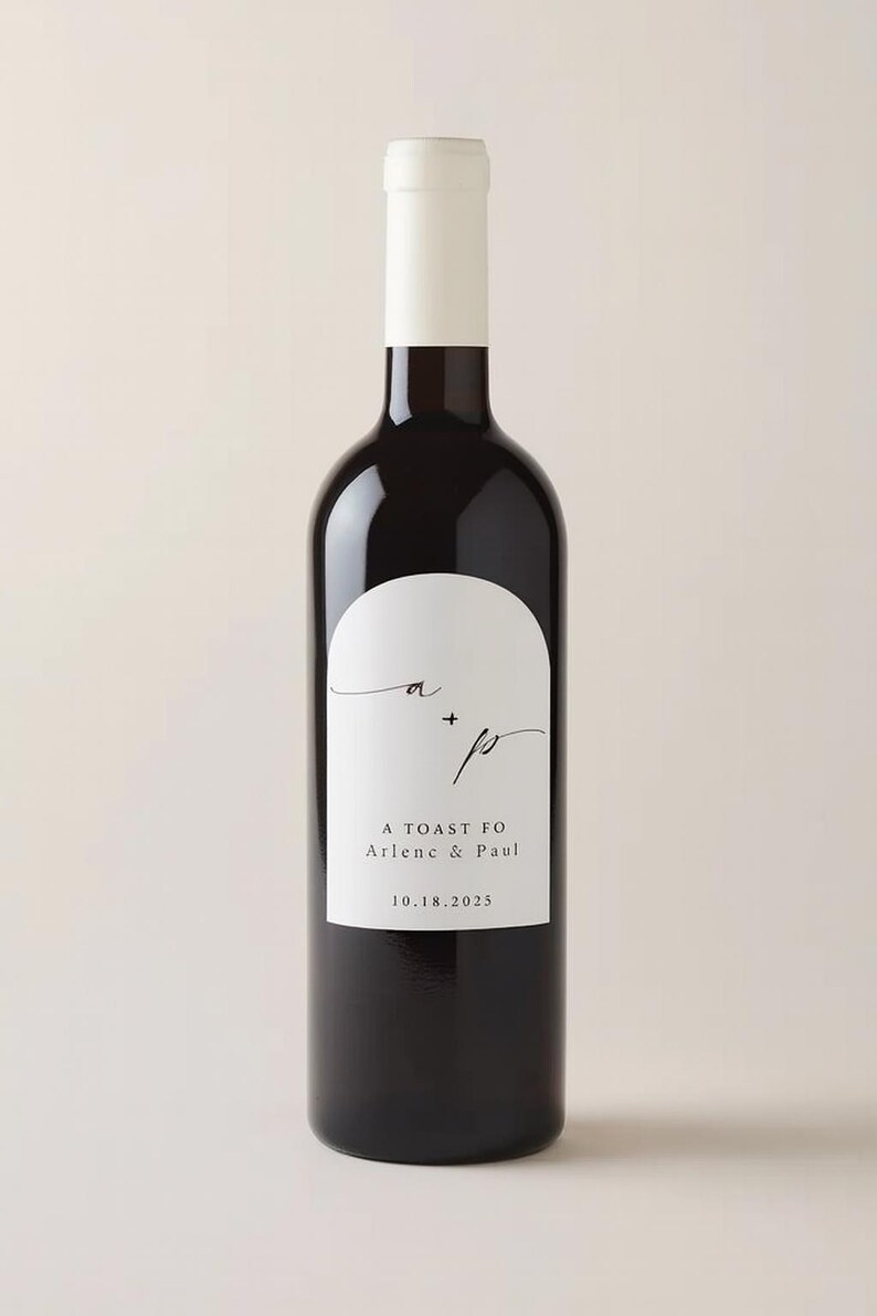May include: A dark wine bottle with a white label featuring the initials "a" and "p" with a plus sign, and the text "A Toast Fo Arlene & Paul 10.18.2025". The bottle has a white top.