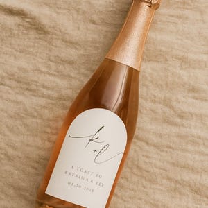 May include: A small bottle of sparkling wine with a rose gold foil top and label. The label has elegant script with the text "A Toast to Katrina K Ley 01.20.2025". The bottle is filled with a light pink liquid, suggesting a ros&eacute; or champagne.