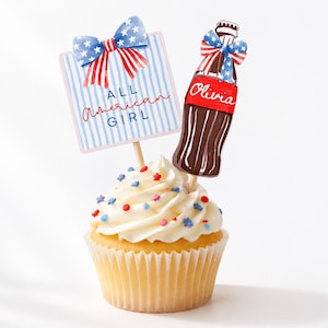 K&ouml;nnte beinhalten: Ein Cupcake mit wei&szlig;em Zuckerguss und bunten Streuseln, gekr&ouml;nt von zwei dekorativen Spie&szlig;en. Einer ist ein Schild mit der Aufschrift "ALL AMERICAN GIRL" und der andere eine Limonadenflasche mit dem Namen "Olivia". Beide Spie&szlig;e haben eine Schleife.