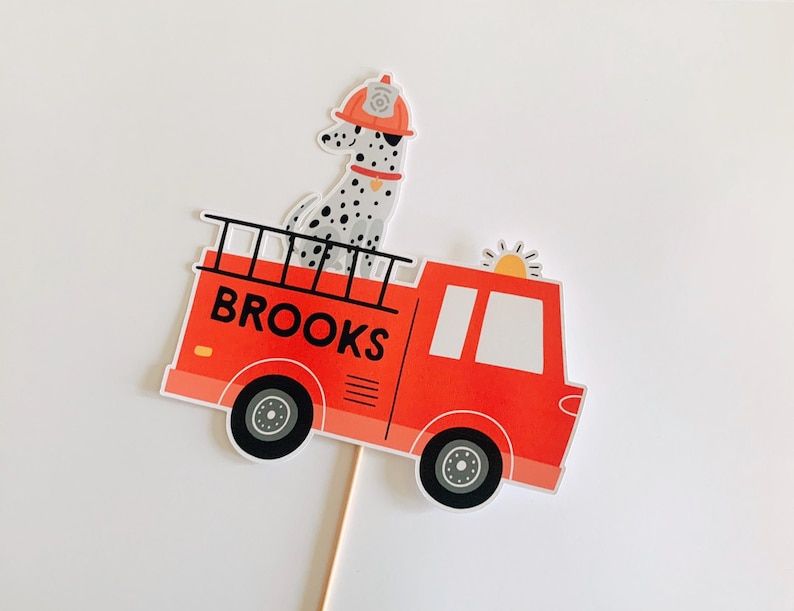 May include: A red fire engine with the name "BROOKS" printed on the side. A Dalmatian dog wearing a firefighter's helmet is on top. The truck has black wheels and a ladder.