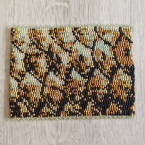 May include: A beaded bracelet featuring a black, gold, and white pattern. The bracelet is crafted with small, round beads and has a scalloped edge.