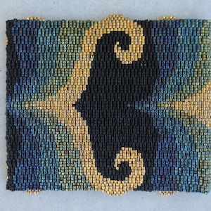 Puede incluir: Un brazalete de cuentas con un diseño negro y dorado. El diseño presenta un patrón de espiral de cuentas negras sobre un fondo de cuentas doradas.