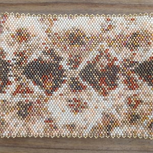 May include: A close-up of a beaded fabric with a pattern of brown, white, and orange beads. The fabric has a scalloped edge.