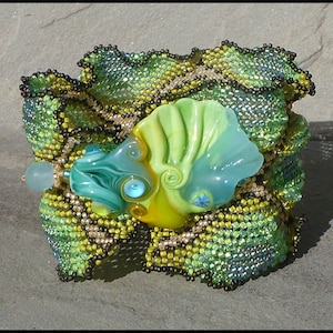 May include: A green, blue, and yellow glass bead with a swirl design is set in a beaded bracelet. The bracelet is made of green, black, and gold beads and has a ruffled edge.