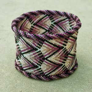 May include: A purple, black and white beaded bracelet with a chevron pattern.