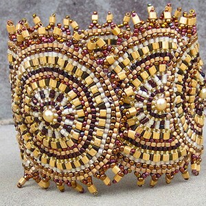 May include: A beaded bracelet with a geometric pattern in shades of brown, gold, and white. The bracelet is made of small, round beads that are arranged in a circular pattern. The beads are sewn together to create a sturdy and durable bracelet.