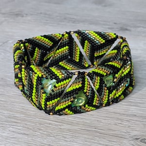 May include: A black, green, and gold beaded bracelet with a geometric pattern. The bracelet is made of small, triangular beads and features a central design of larger, faceted beads.