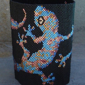 May include: A black beaded bracelet with a blue, gold, and pink gecko design.