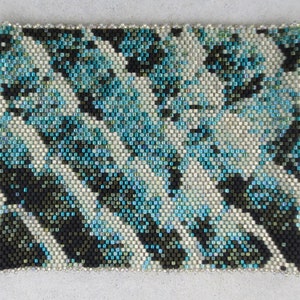 May include: A close-up of a beaded bracelet with a black, white and blue geometric pattern.