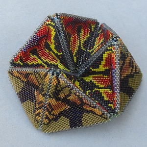 Könnte beinhalten: Eine geometrische, origamiartige Schachtel aus Perlen mit einem farbenfrohen, abstrakten Muster in Gelb-, Orange-, Rot-, Schwarz- und Silbertönen.