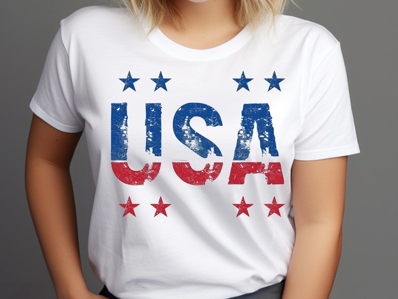 May include: White t-shirt with a distressed red, white, and blue "USA" graphic. The graphic is surrounded by six red stars.