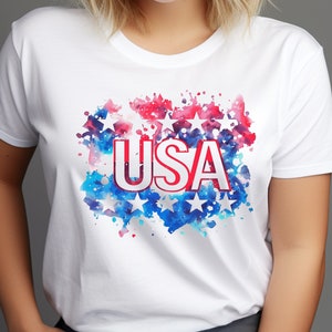 May include: White t-shirt with a red, white, and blue watercolor design featuring stars and the word "USA".