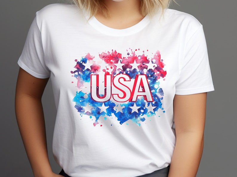 May include: White t-shirt with a red, white, and blue watercolor design featuring stars and the word "USA".