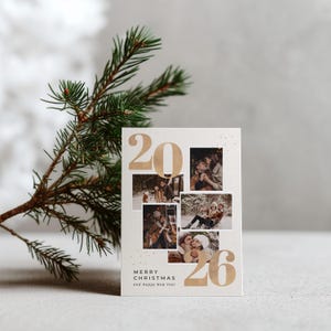 May include: A holiday greeting card with the numbers "2026" in gold, featuring multiple photos. The card includes the text "MERRY CHRISTMAS and Happy New Year" in a script font. A sprig of evergreen is in the background.