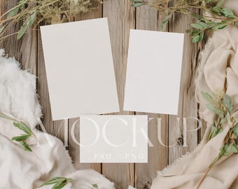 May include: A mockup scene featuring three blank white cards and a folded card on a rustic wooden surface. The scene is decorated with beige fabric, green leaves, and dried flowers. The text "MOCKUP" and "PSD / PNG" are visible.