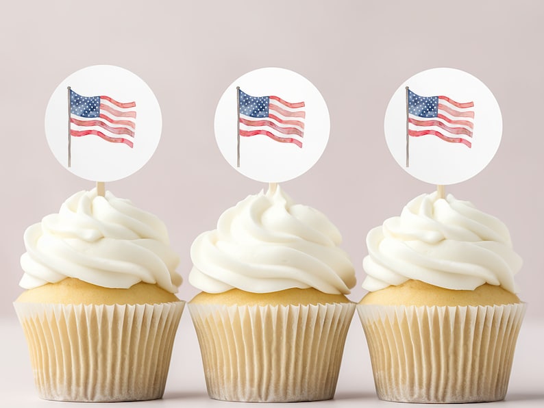 May include: Three cupcakes with white frosting topped with round paper circles featuring a watercolor American flag design.