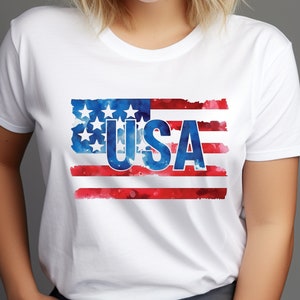 May include: White t-shirt with a watercolor design of the American flag and the word "USA" in blue letters.