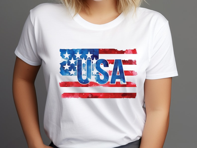 May include: White t-shirt with a watercolor design of the American flag and the word "USA" in blue letters.