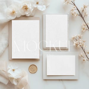 May include: A mockup featuring three white cards in different sizes, arranged on a light surface. The cards are set in light gray frames. A gold wax seal and white flowers with yellow centers are also present, creating an elegant, minimalist aesthetic.