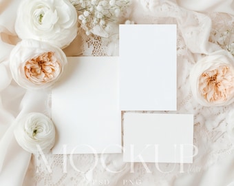May include: A mockup featuring three blank white cards of varying sizes, arranged on a cream-colored lace and fabric background. White and peach-colored roses and small white flowers are scattered around the cards. The word "MOCKUP" is visible.