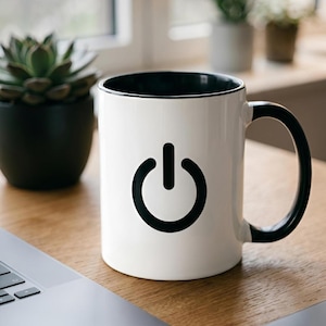 Pode incluir: Uma caneca de cerâmica branca com um símbolo de botão de energia preto na parte frontal. A caneca possui um interior preto e uma alça preta. O design está centralizado na superfície externa da caneca, proporcionando uma representação clara.