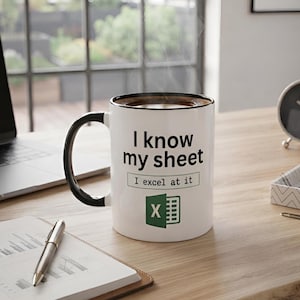 May include: A white ceramic mug with a black handle and rim, featuring the black text "I know my sheet" above a box containing the text "I excel at it" and a green Microsoft Excel icon. The mug contains a dark brown liquid with visible steam.