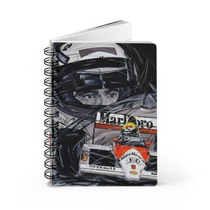 May include: Spiral-bound notebook featuring a detailed illustration of a Formula 1 race car and driver. The artwork is predominantly black, white, and red, with the word "Marlboro" visible. The notebook's design captures the essence of motorsports.