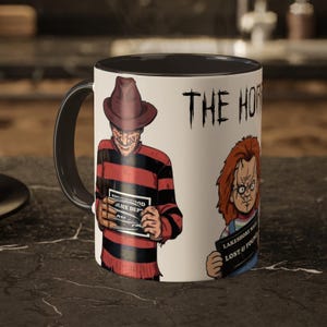Puede incluir: Taza de cerámica blanca con borde y asa negros. La taza presenta un gráfico de Freddy Krueger y Chucky de las películas de terror. El texto "The Horror" está impreso en la taza.
