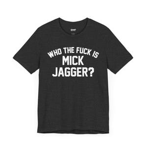 Puede incluir: Camiseta gris oscuro con el texto blanco "WHO THE FUCK IS MICK JAGGER?" en letras mayúsculas en negrita. La camiseta tiene cuello redondo y mangas cortas. La tela parece suave y cómoda.