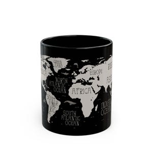 May include: Black ceramic mug featuring a world map design in white. The map includes continents and oceans labeled with text. A stylish and functional item for enjoying beverages.