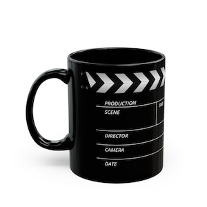 Puede incluir: Taza de cerámica negra con un diseño de claqueta de cine. La taza presenta un patrón de chevrón blanco y campos de texto para detalles de producción. El asa es curva y de color negro sólido. La taza está diseñada para bebidas.