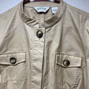 May include: Tan-colored jacket with a mandarin collar and two front pockets. The jacket has large, decorative buttons and the brand name "ORVIS" on the label.