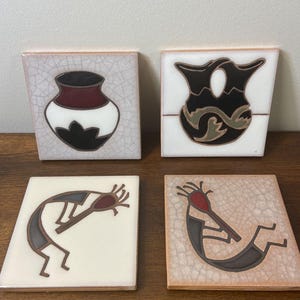 May include: Set of four square ceramic tiles with Southwestern designs. Each tile features a different image: a vase, a double vase, and two Kokopelli figures. The tiles have a crackle finish and are in shades of white, brown, black, and red.