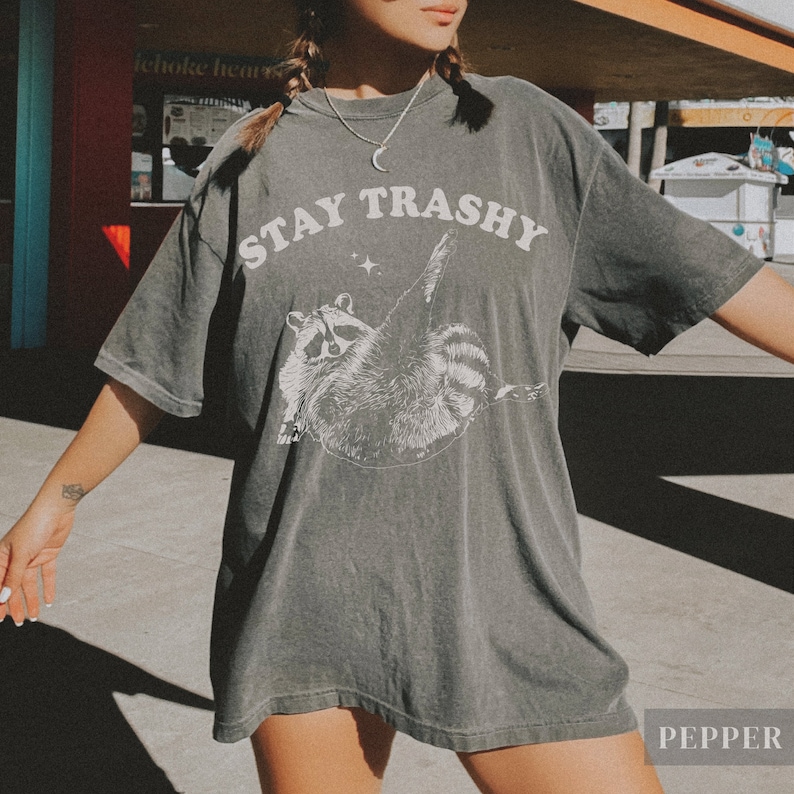 May include: A dark gray oversized t-shirt with a white graphic of a raccoon and the text "STAY TRASHY".