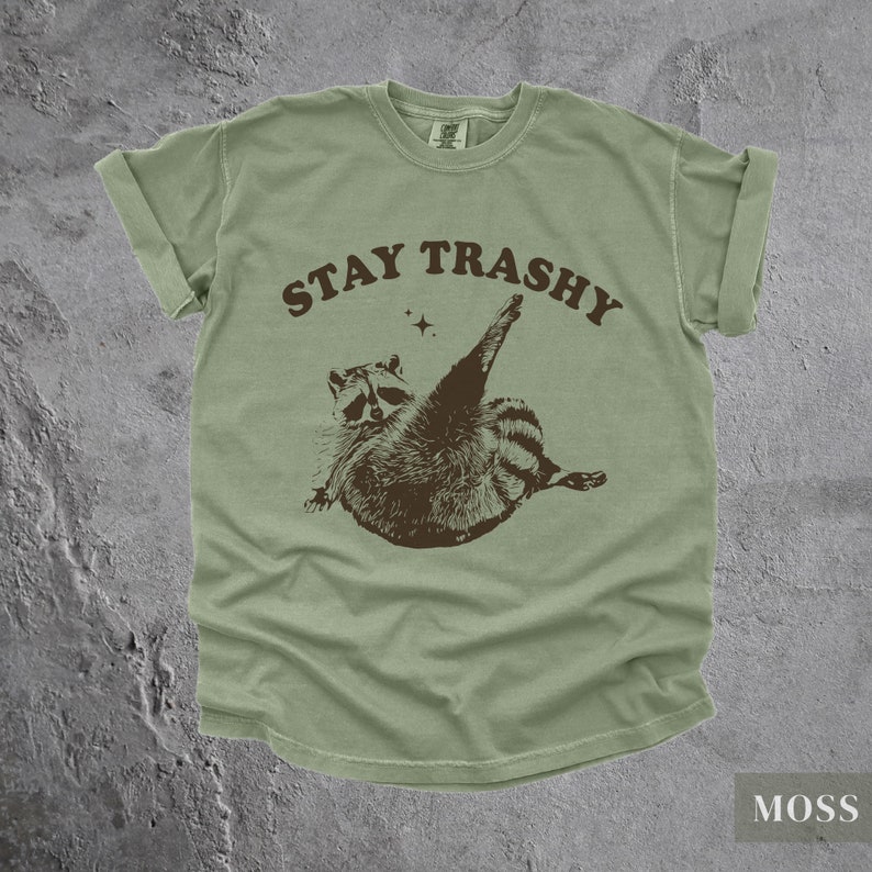 May include: A green t-shirt with a brown raccoon graphic and the text "STAY TRASHY" in brown letters.