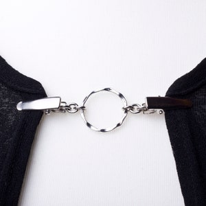May include: A silver chain with two clips and a decorative ring, used to hold a garment together.