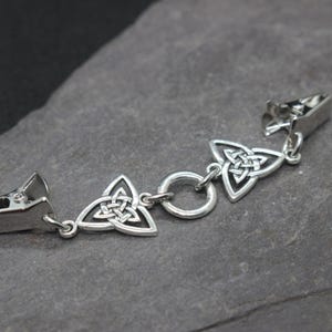 Puede incluir: Una pulsera de metal plateado con un dise&ntilde;o de nudo celta. La pulsera presenta tres dijes triangulares de nudo celta y dos cierres de clip. El dise&ntilde;o es sim&eacute;trico y el metal tiene un acabado pulido.