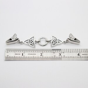 Puede incluir: Un clip de chal de nudo celta de metal plateado. El clip tiene dos extremos con un cierre y un dise&ntilde;o de nudo celta, conectados por un anillo. Mide aproximadamente 10 cm de largo.