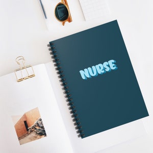 Könnte beinhalten: Ein dunkelblaues Spiralnotizbuch mit dem Wort "NURSE" in hellblauen Buchstaben. Das Notizbuch ist geschlossen und liegt auf einer weißen Oberfläche.