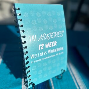 May include: A blue spiral bound workbook titled "The Mujeres 12 Week Wellness Workbook" by Heather Anita Garcia. The cover features a repeating pattern of white lemons.