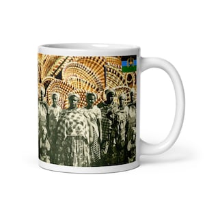 May include: White ceramic mug featuring a colourful image of a group of people wearing traditional clothing and holding baskets. The background is a pattern of woven baskets. The mug has a blue and yellow flag with a star on it.