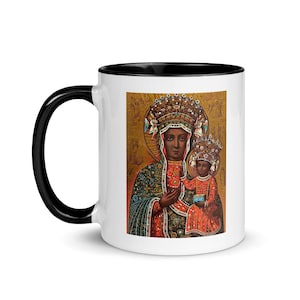 Könnte beinhalten: Weiße Keramiktasse mit schwarzem Henkel und Innenraum. Die Tasse zeigt eine religiöse Ikone einer dunkelhäutigen Frau und eines Kindes mit Kronen und verzierten Gewändern. Der Hintergrund ist goldfarben.