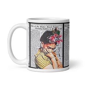 May include: White ceramic mug featuring a portrait of a woman with flowers in her hair, set against a newspaper-style background. The text on the mug reads "Wife of the Master Mural Painter Gleefully Dabbles in Wo of Art."