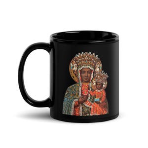 Könnte beinhalten: Schwarze Keramiktasse mit einem religiösen Bild einer Frau und eines Kindes, beide mit Kronen und aufwendiger Kleidung. Das Bild ist vor einem goldenen Heiligenschein platziert und kontrastiert mit der dunklen Oberfläche der Tasse. Klassische Kaffeetasse.