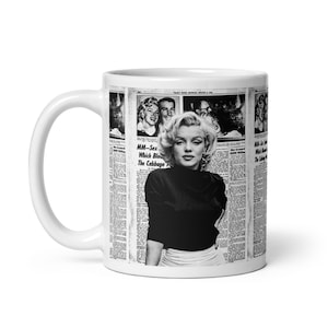 Può includere: Tazza in ceramica bianca con un'immagine in bianco e nero di Marilyn Monroe. L'immagine è ambientata su uno sfondo di ritagli di giornale. La tazza ha un manico curvo e una finitura lucida.