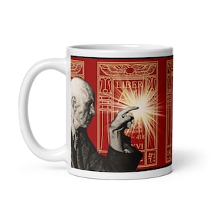 Może przedstawiać: Biały ceramiczny kubek z czarno-białym wizerunkiem mężczyzny wskazującego na jasne światło. Projekt kubka obejmuje czerwone tło ze złotymi ilustracjami w stylu hieroglifów i słowem "LIBER".