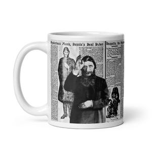 May include: White ceramic mug featuring a black and white image of Rasputin with the text "Mysterious Monk, Russia's Real Ruler" and newspaper-style background. The mug has a curved handle.